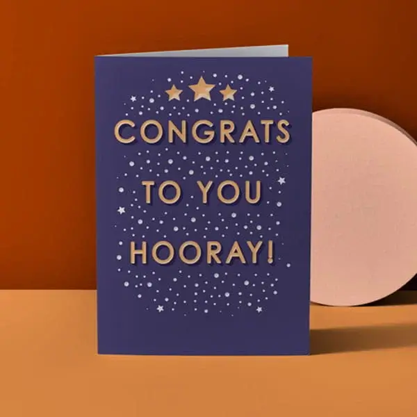 Congratulations card with gold foil lettering, star accents, and Hooray message on a dark blue background.